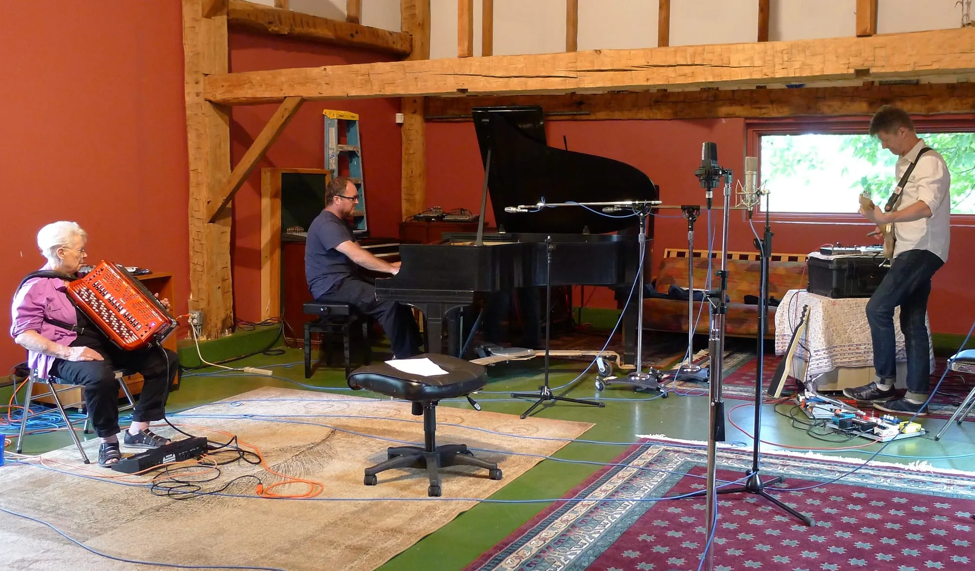 Pauline Oliveros wearing headphones and playing accordion beside Nels Cline and Thollem McDonas during a 2015 recording session.